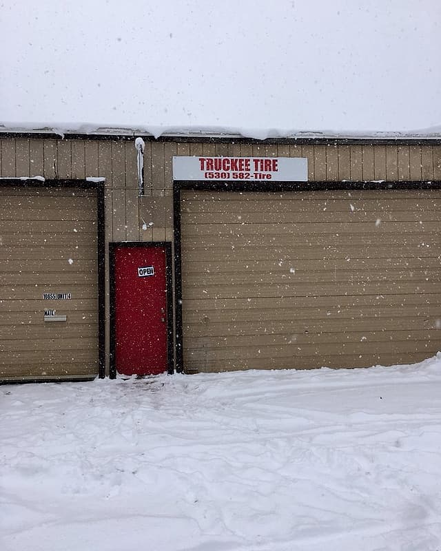 The old Truckee Tire shop in a snowstorm: a white sign over closed bay doors and a red door with an Open sign